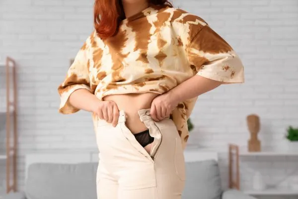 Image of woman trying to do her trousers up after pregnancy weight gain Birmingham